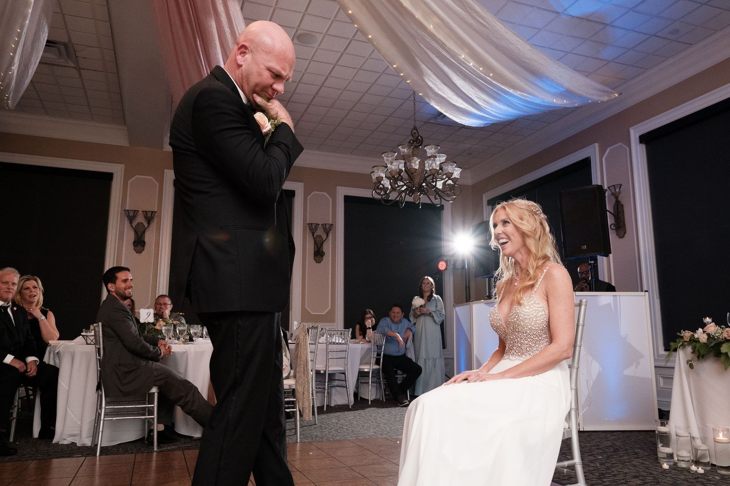 Wedding couple dances together during their first dance at an elegant white-decorated reception venue.