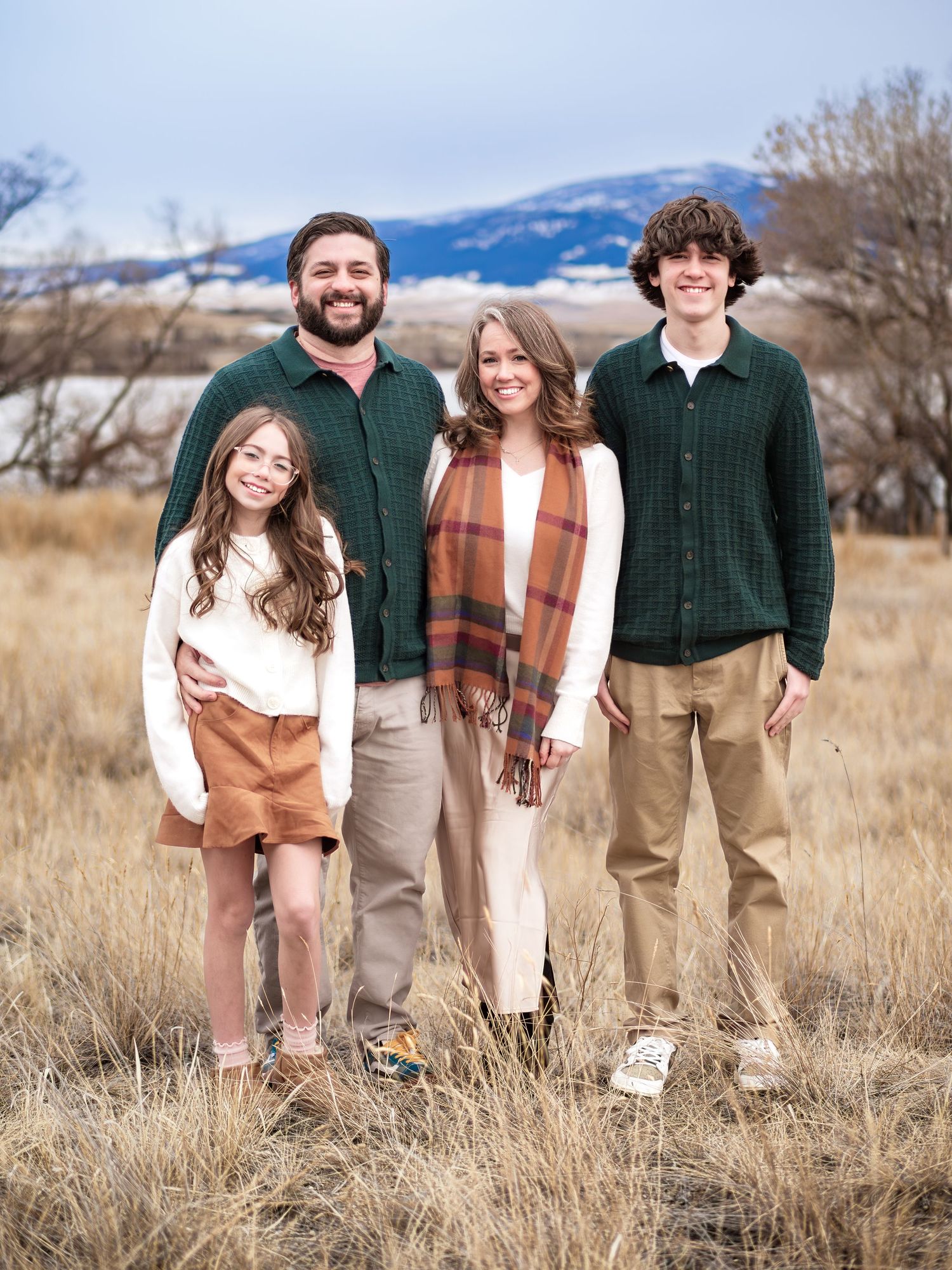 Family of four in casual attire posing in field with mountains in background.