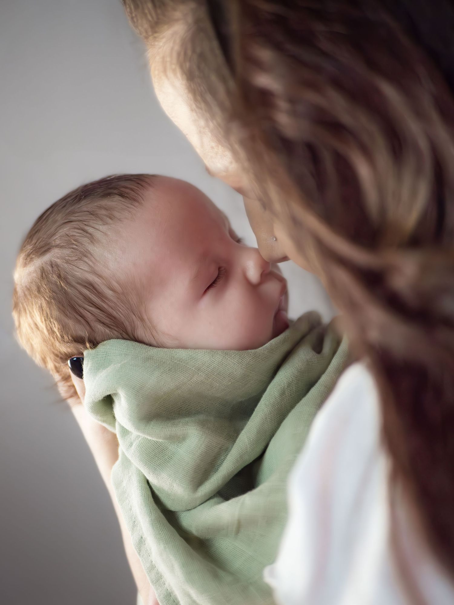 A tender moment between parent and infant swaddled in soft mint green fabric.