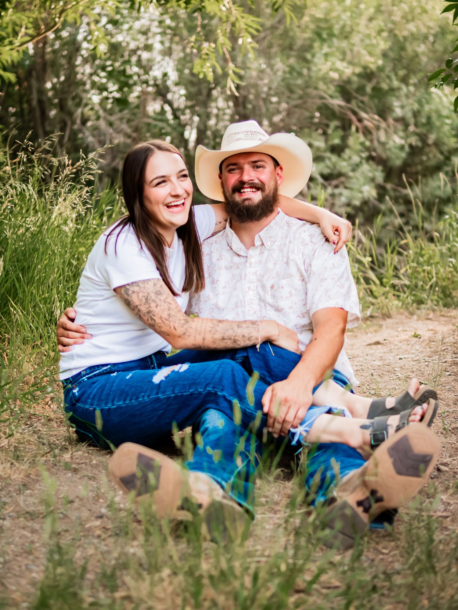 Couple in casual western wear sharing a laugh while sitting on trail.
