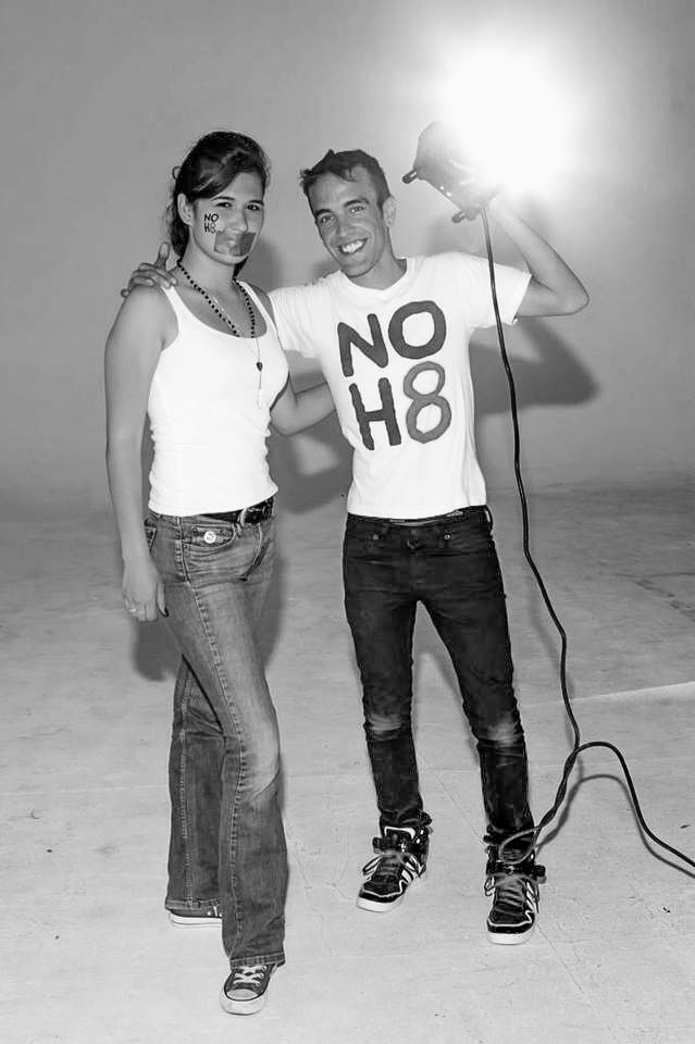 Two people posing against white background, one wearing NO H8 shirt.