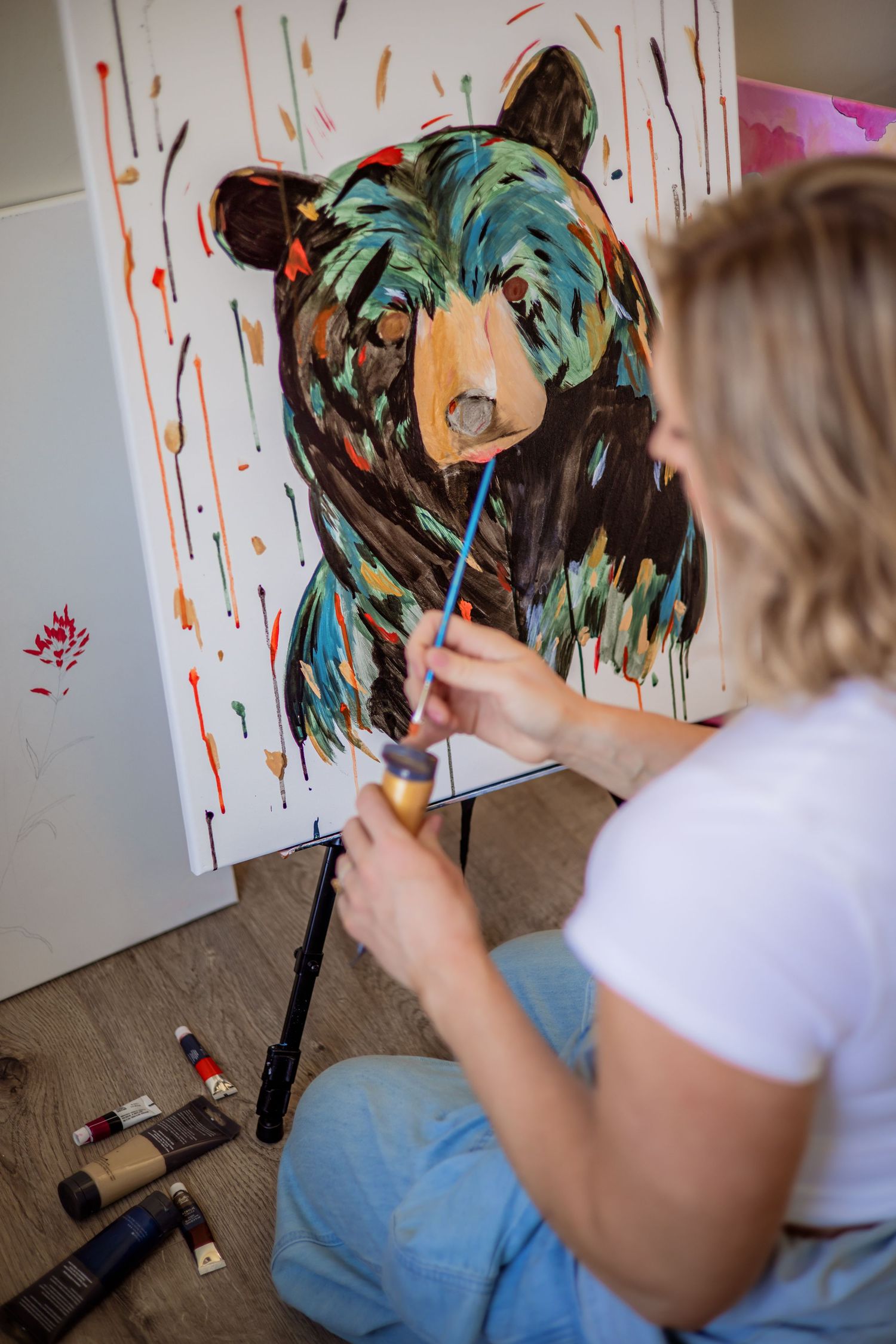 Artist painting a vibrant turquoise and orange bear portrait on canvas.