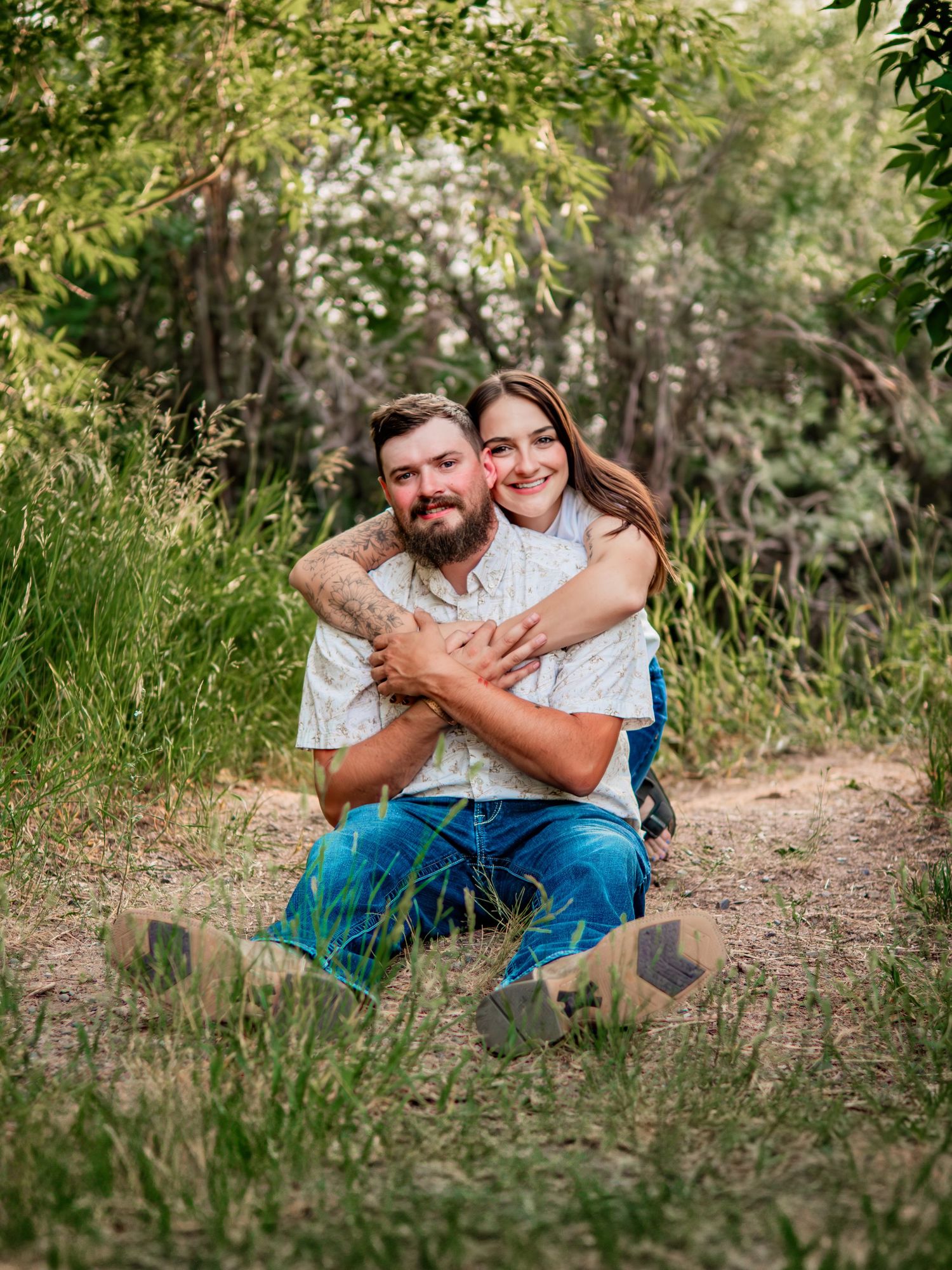 Couple embracing on nature trail surrounded by green foliage.