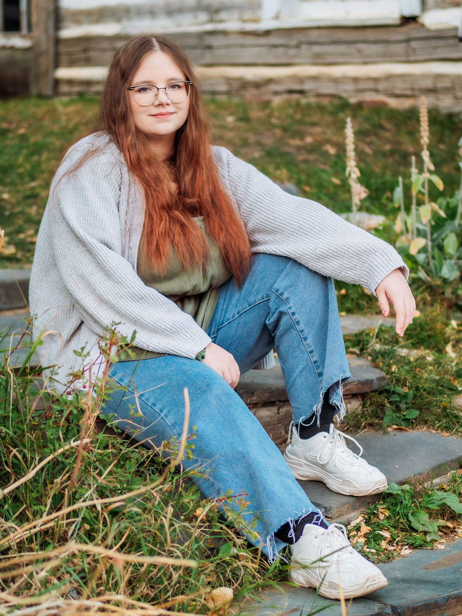 Casual portrait of person in oversized sweater sitting outdoors near garden.