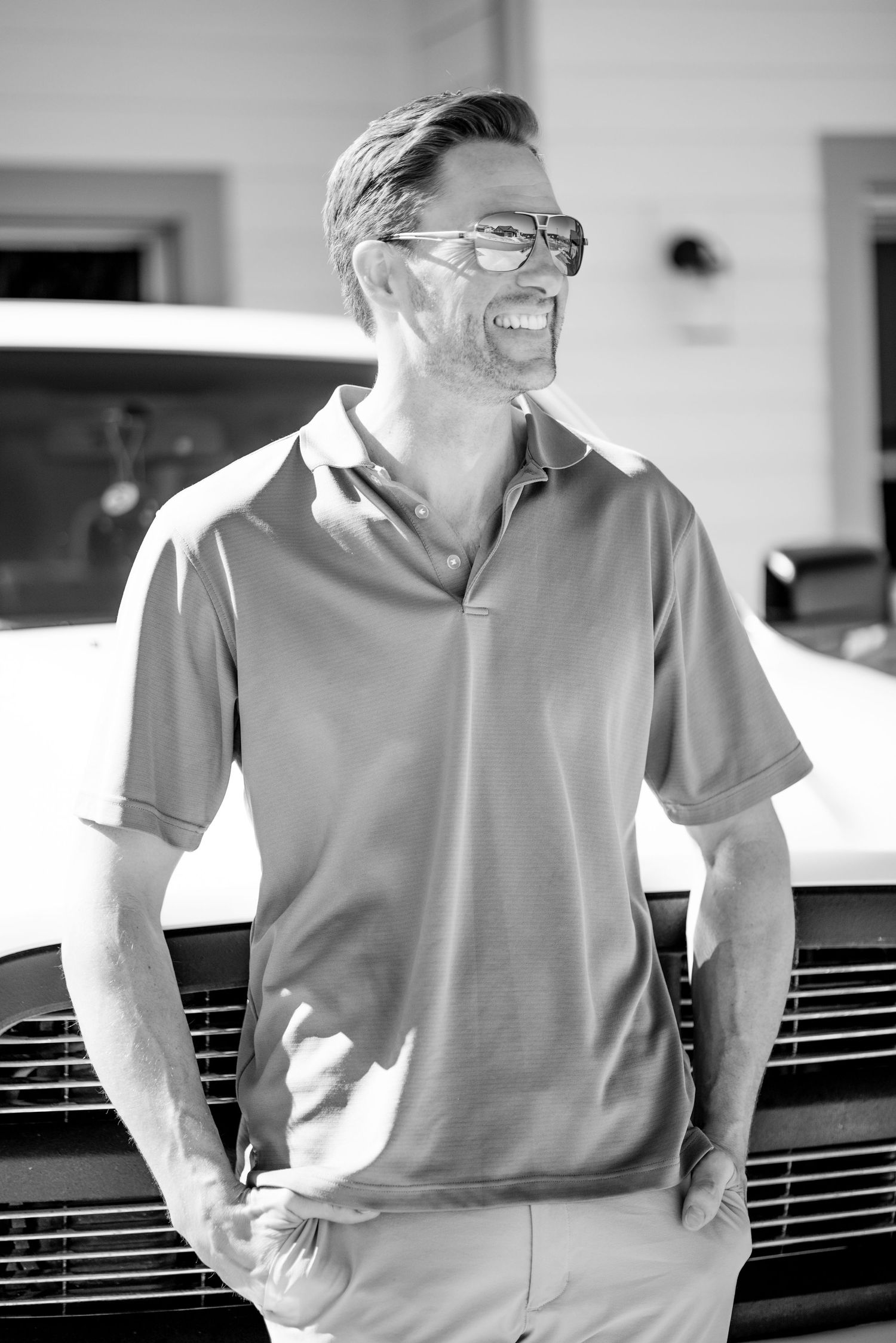 Casual portrait of person in polo shirt leaning against car and laughing.