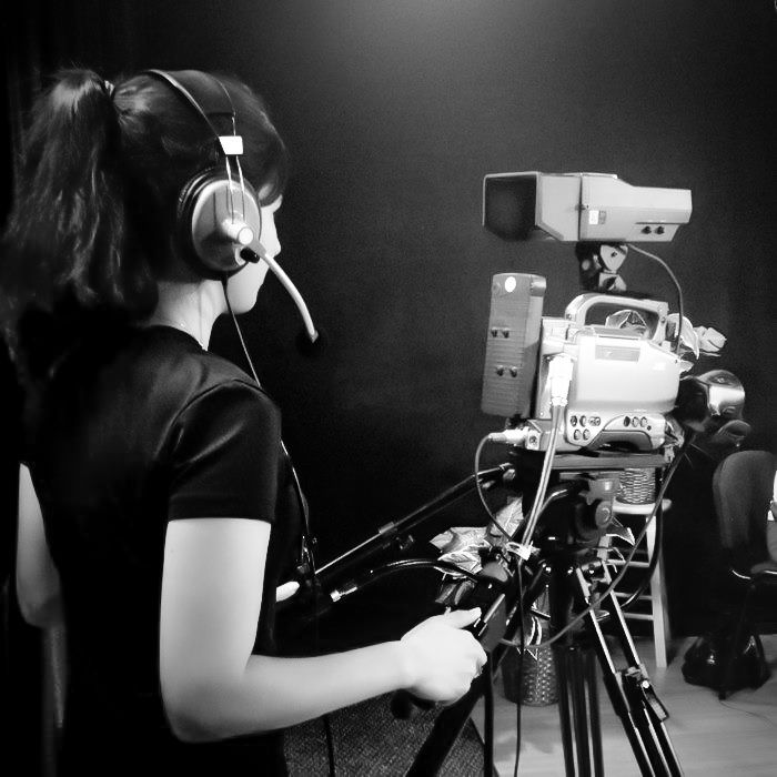Camera operator filming with professional equipment in dark studio setting.