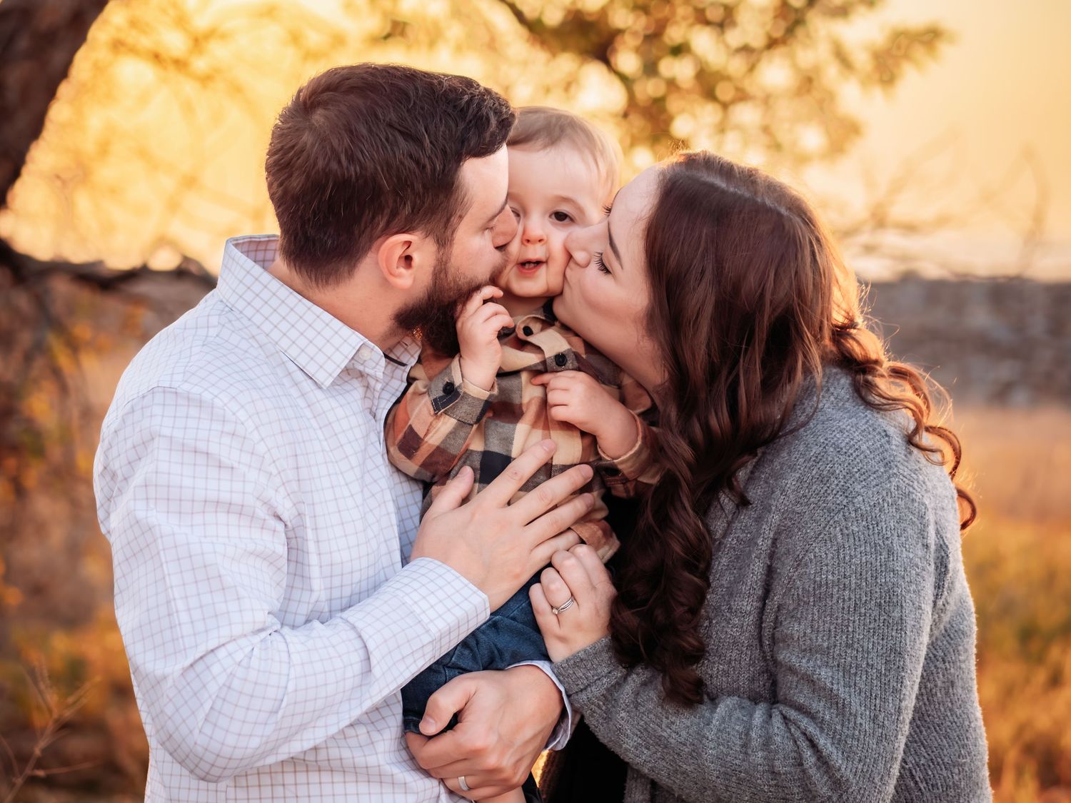 A happy family of three sharing a joyful autumn moment together outdoors during golden hour.