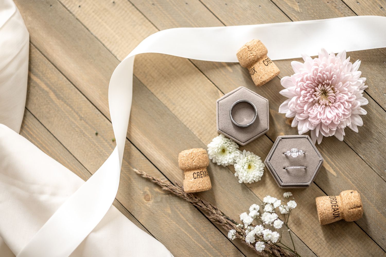 Overhead view of hexagonal glass jars, wine corks, pink chrysanthemum and baby's breath flowers on wooden decking.