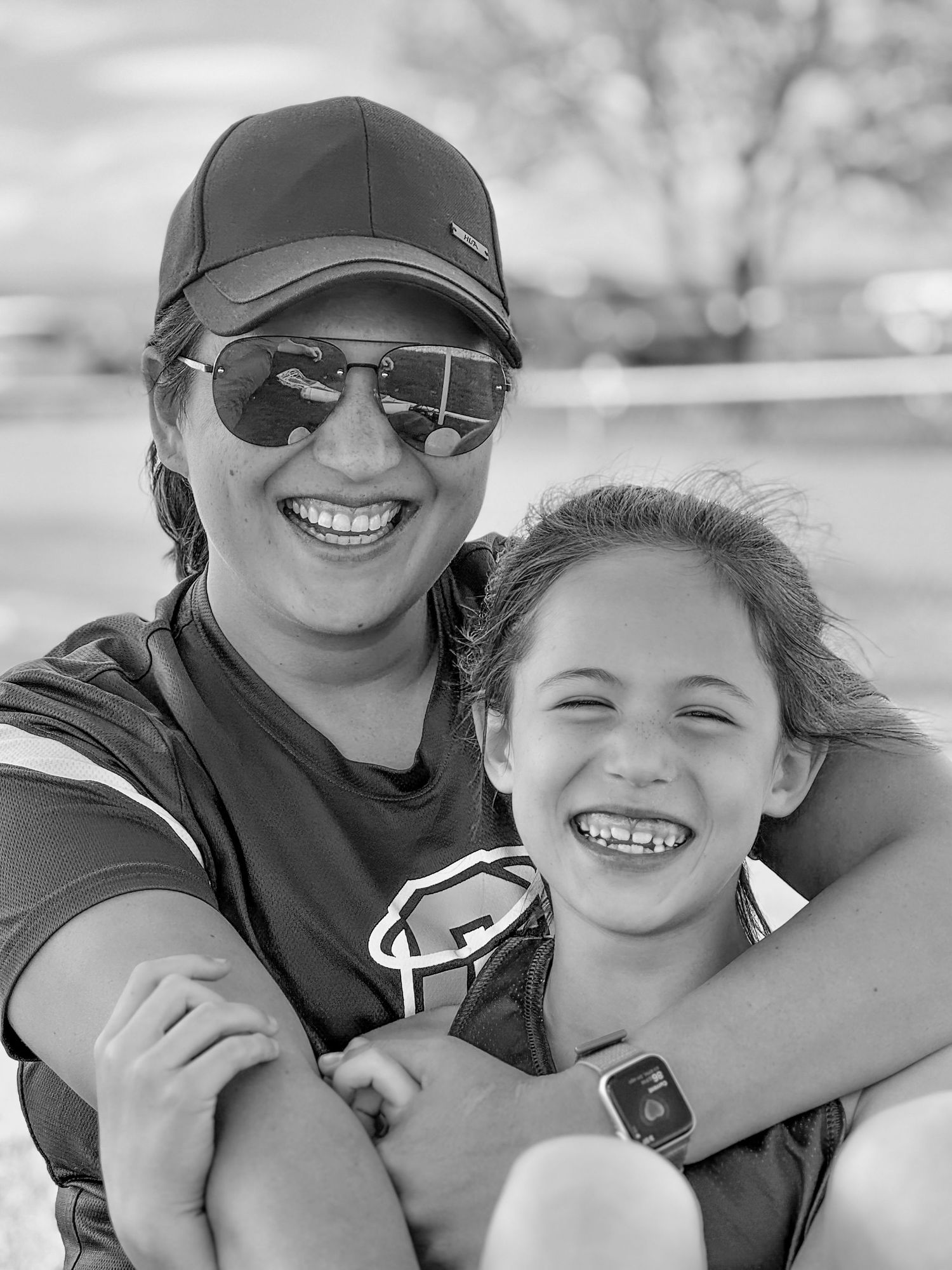 Parent and child taking cheerful selfie together outdoors wearing baseball caps.