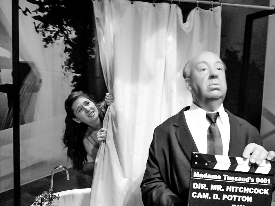 Behind-the-scenes photo of Alfred Hitchcock on movie set with clapboard.