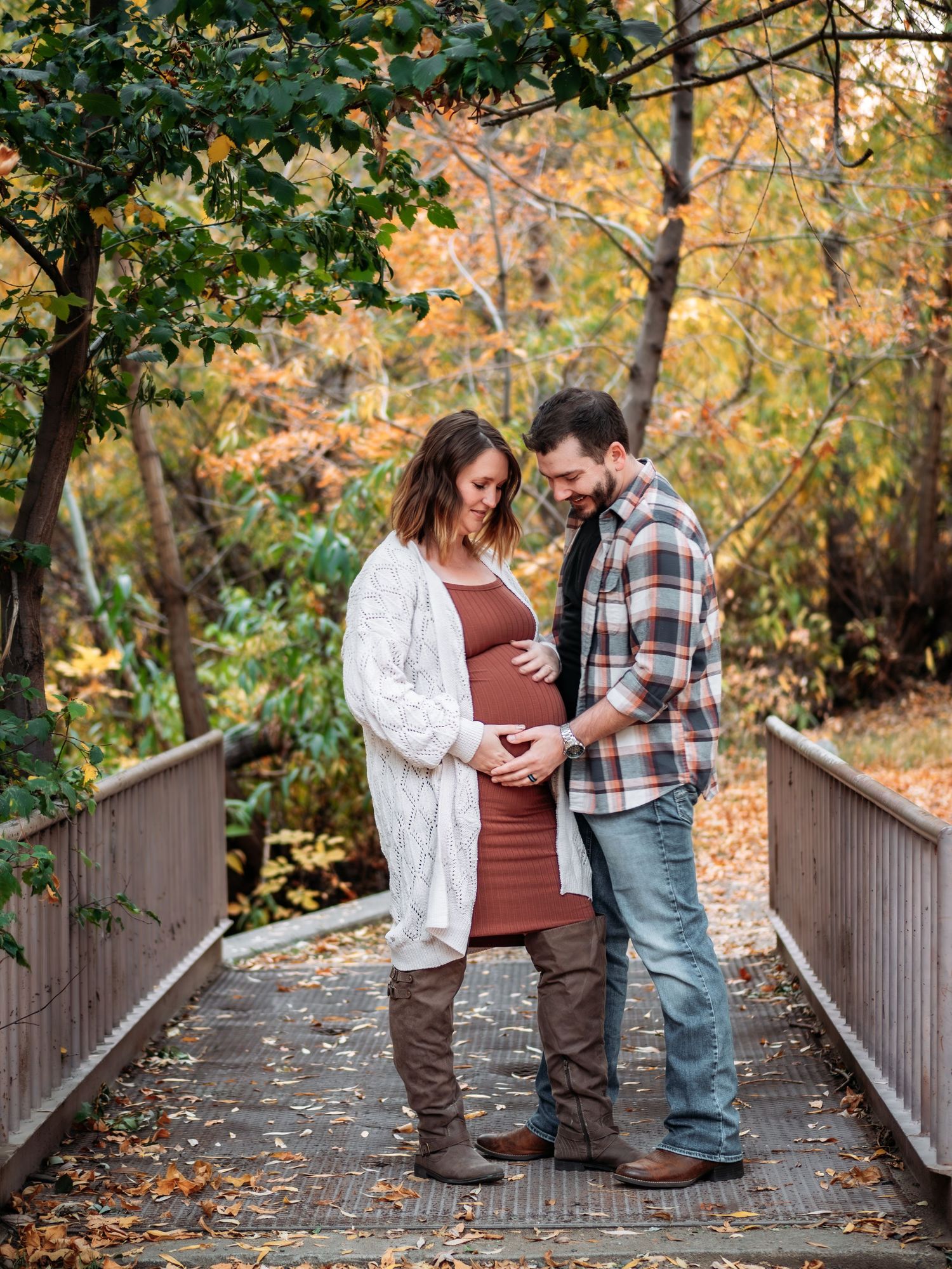 Couple embracing on wooden bridge surrounded by autumn foliage.
