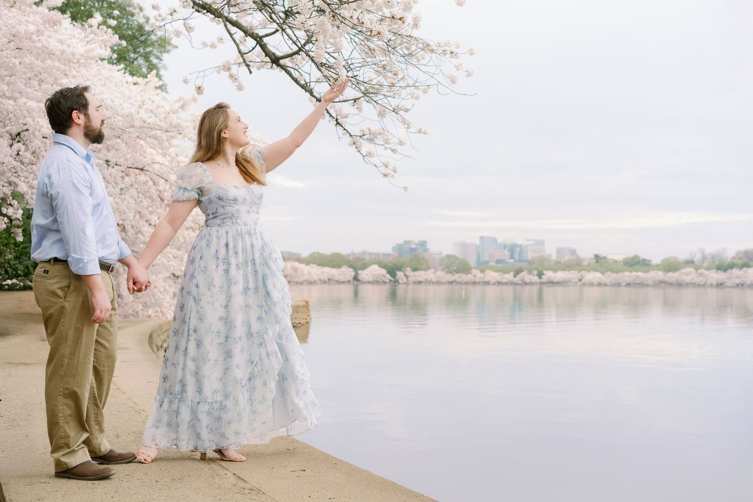 A couple admires cherry blossoms while standing along the Tidal Basin pathway.