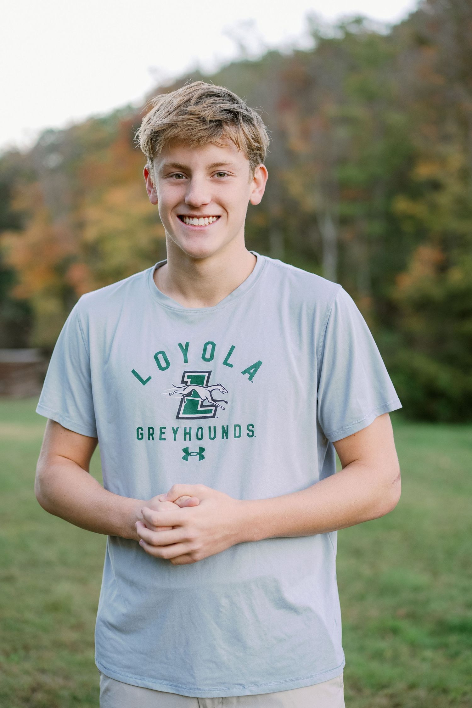 A person wearing a gray Loyola Greyhounds t-shirt smiles while sitting outdoors in a natural setting.