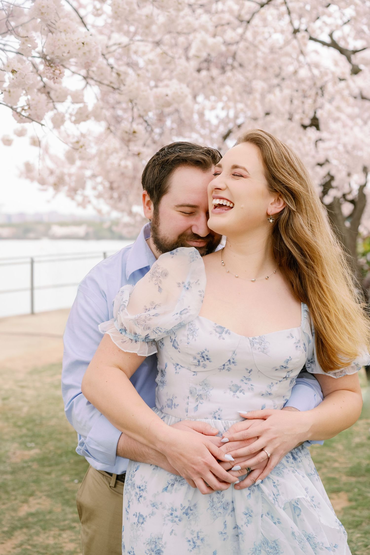 Romantic moment shared between couple under blooming cherry blossom trees near waterfront.