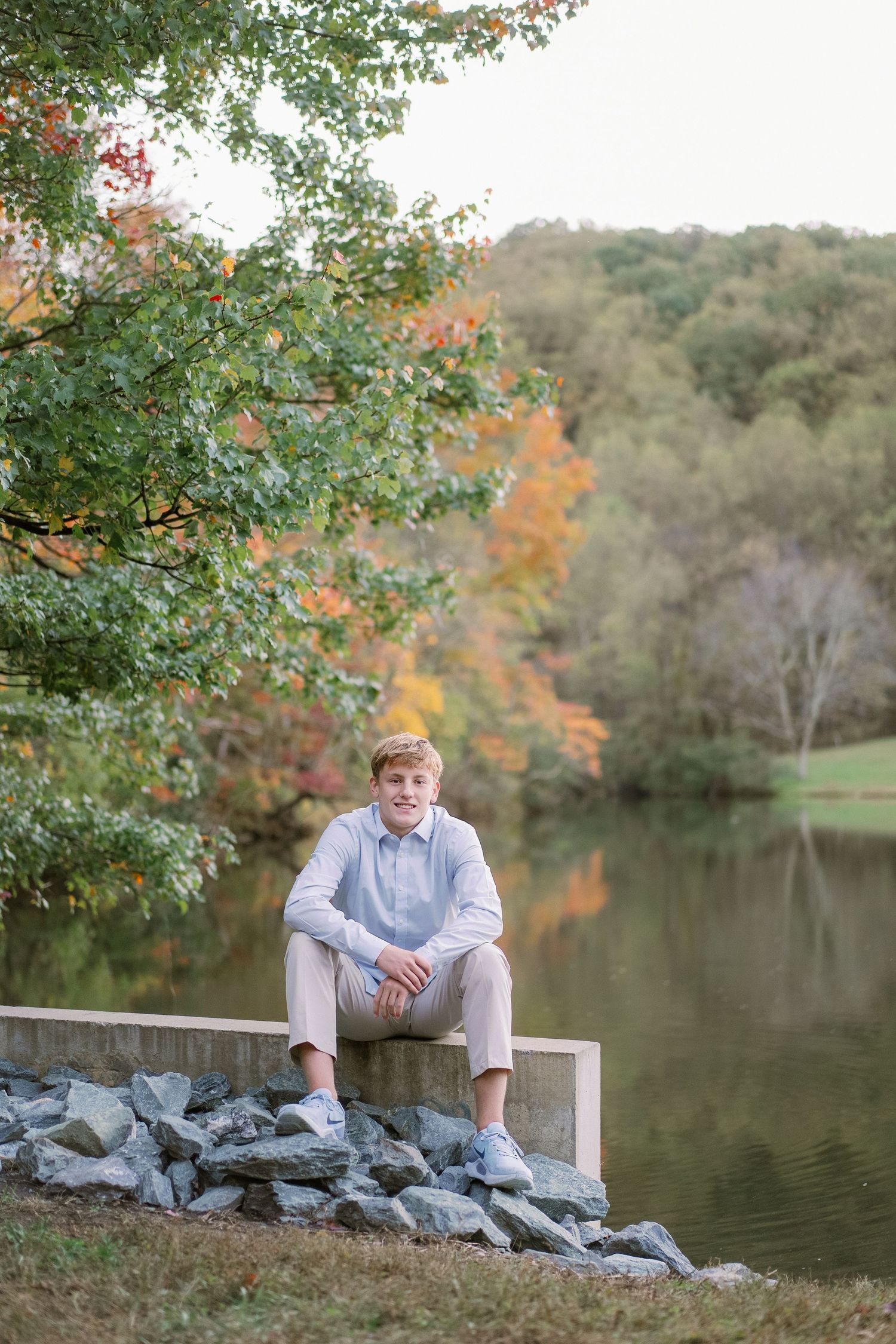 A tranquil lakeside scene in autumn with someone sitting on a white bench surrounded by colorful foliage and rocks.