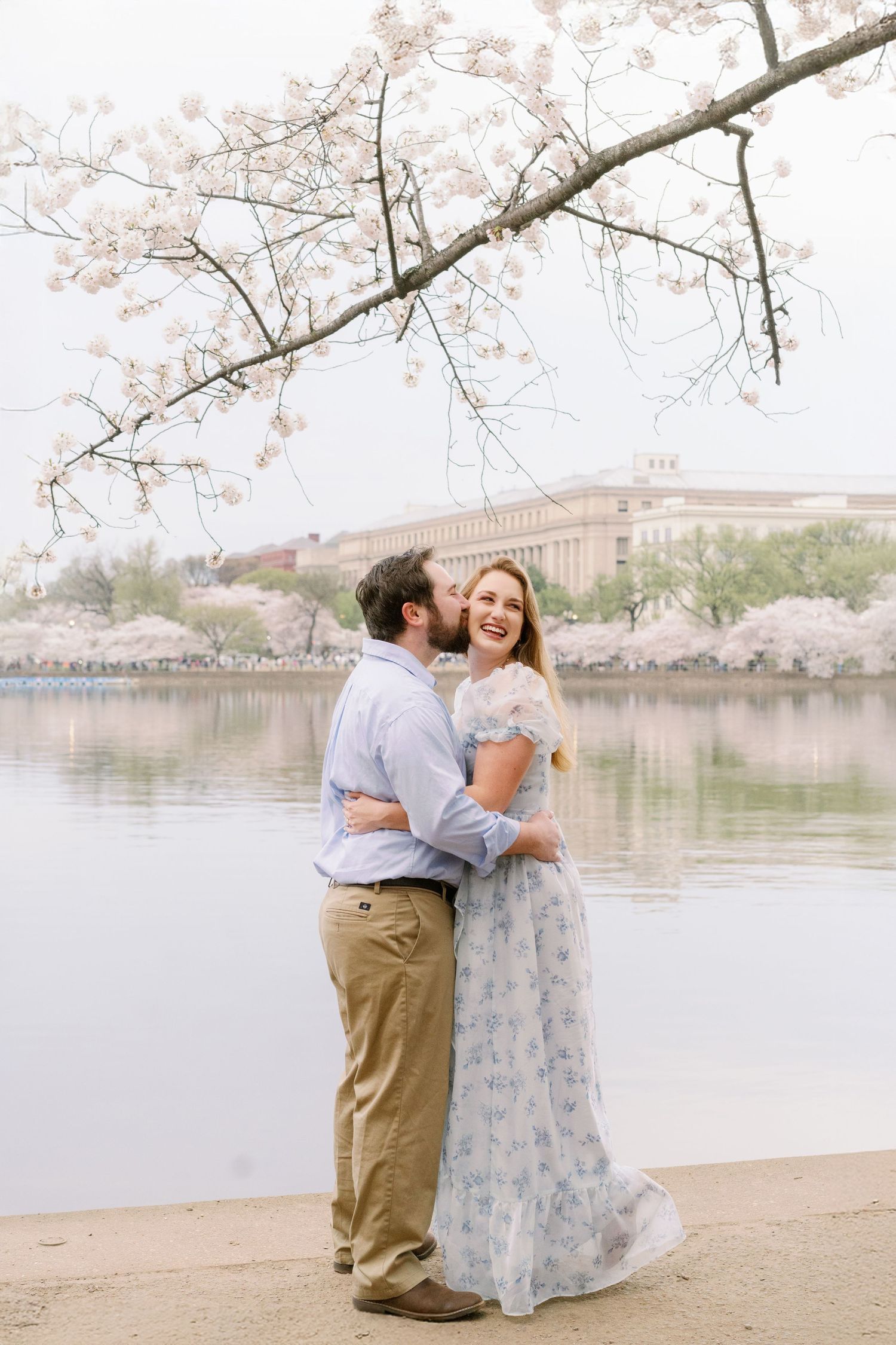 A tender embrace under cherry blossom branches beside the Tidal Basin in springtime.