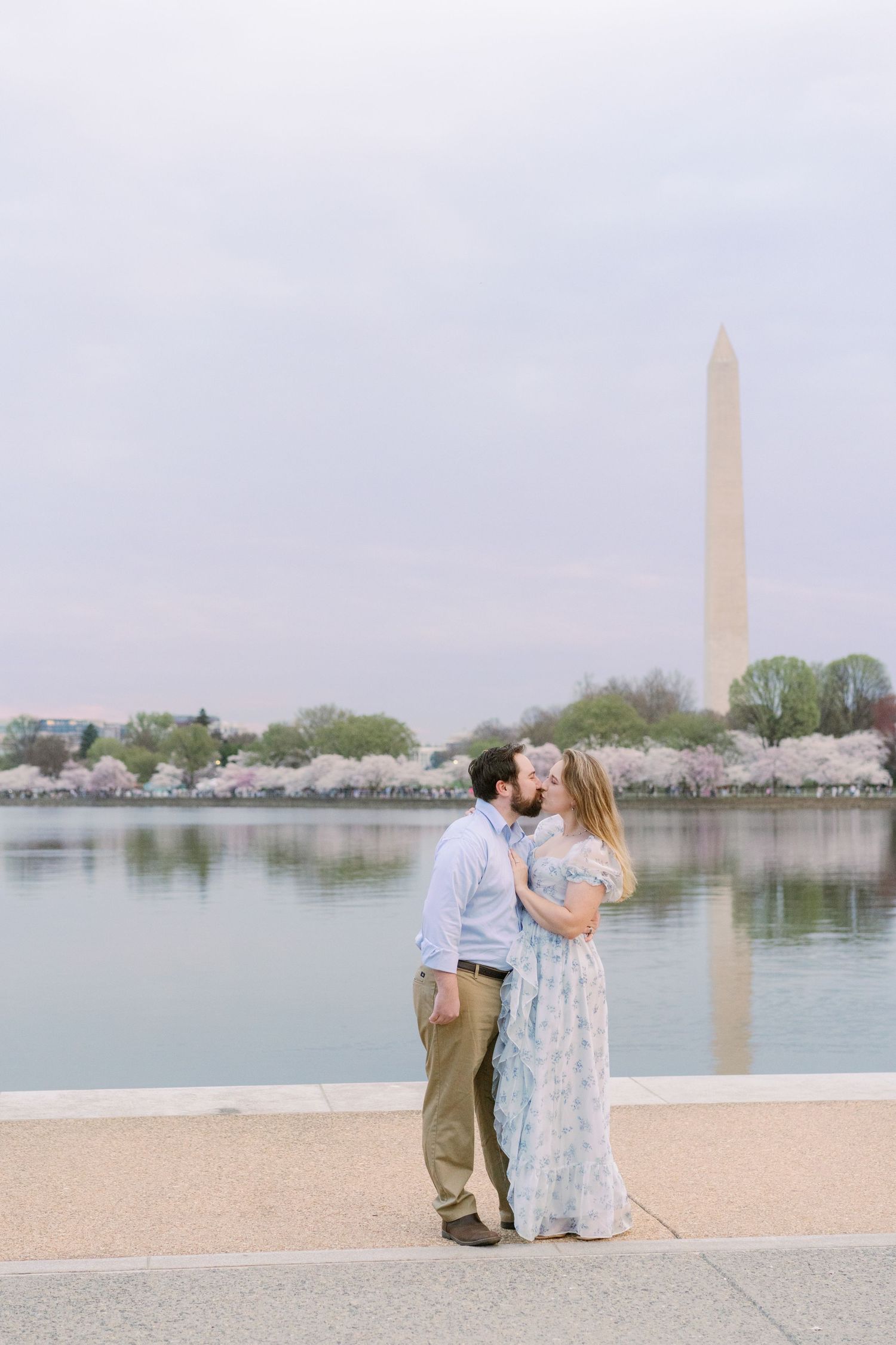Couple in spring attire embracing near Washington Monument during cherry blossom season.