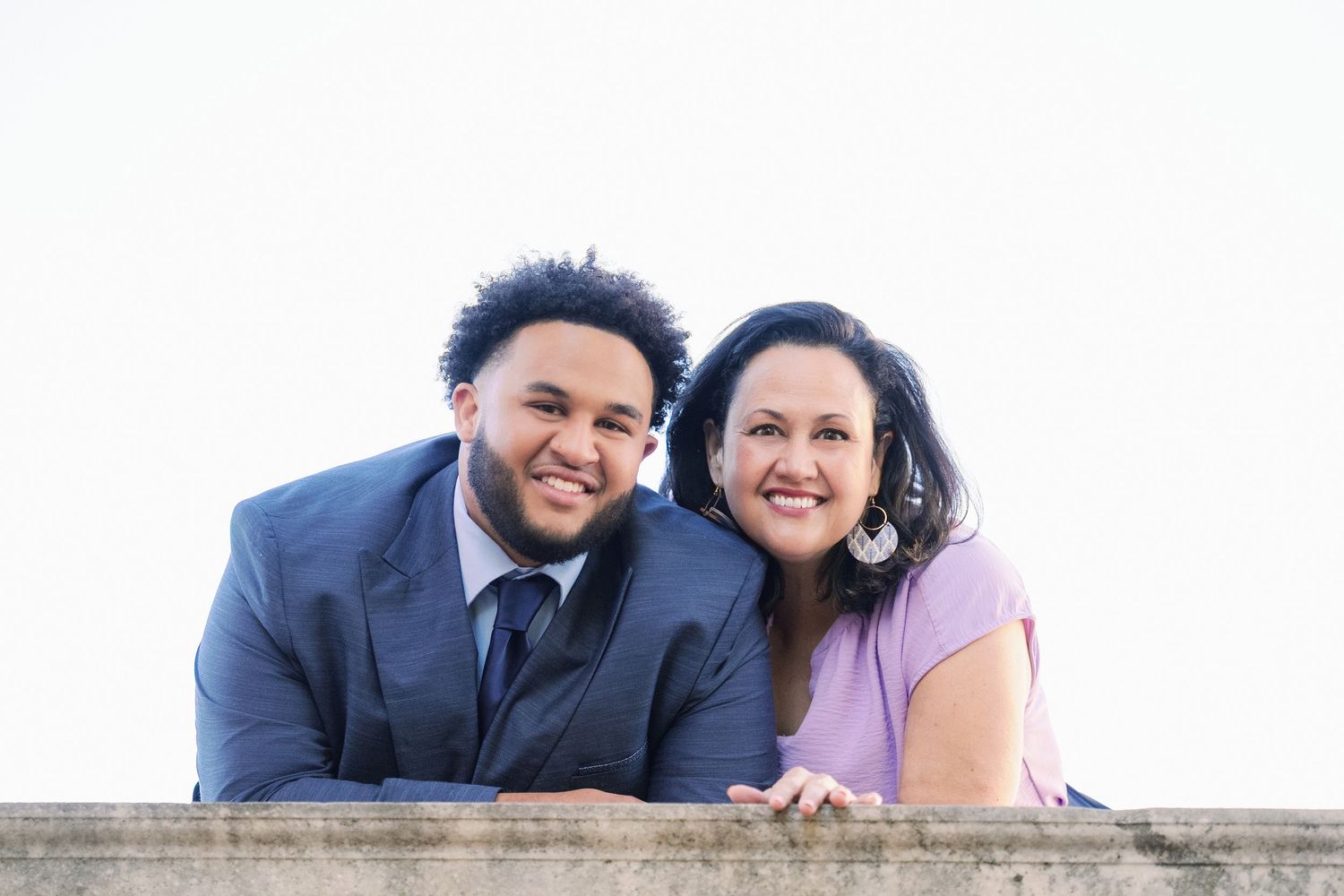 Couple lying on wooden deck in casual attire smiling during outdoor photo session.