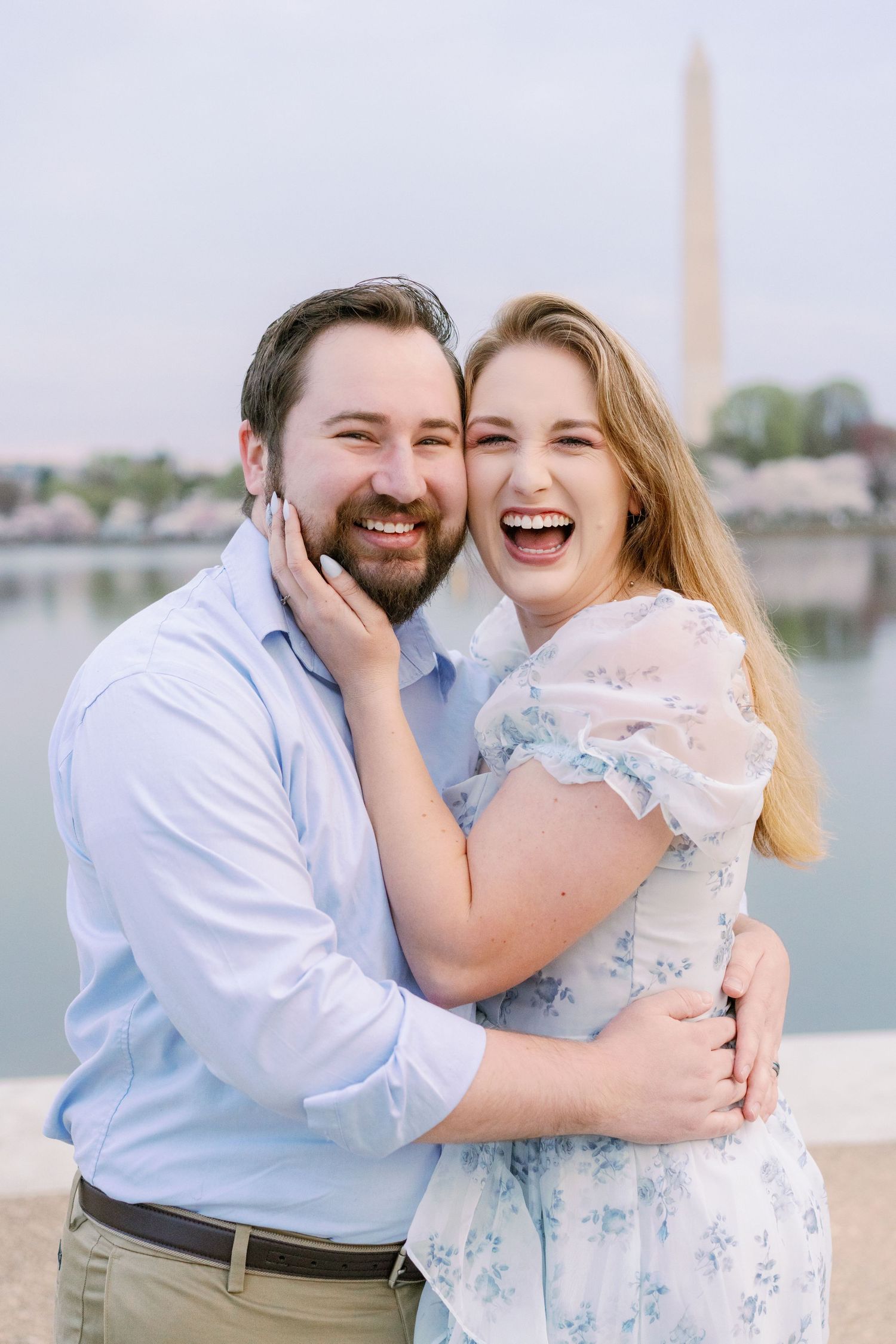 Joyful couple embracing by Washington Monument during cherry blossom season.