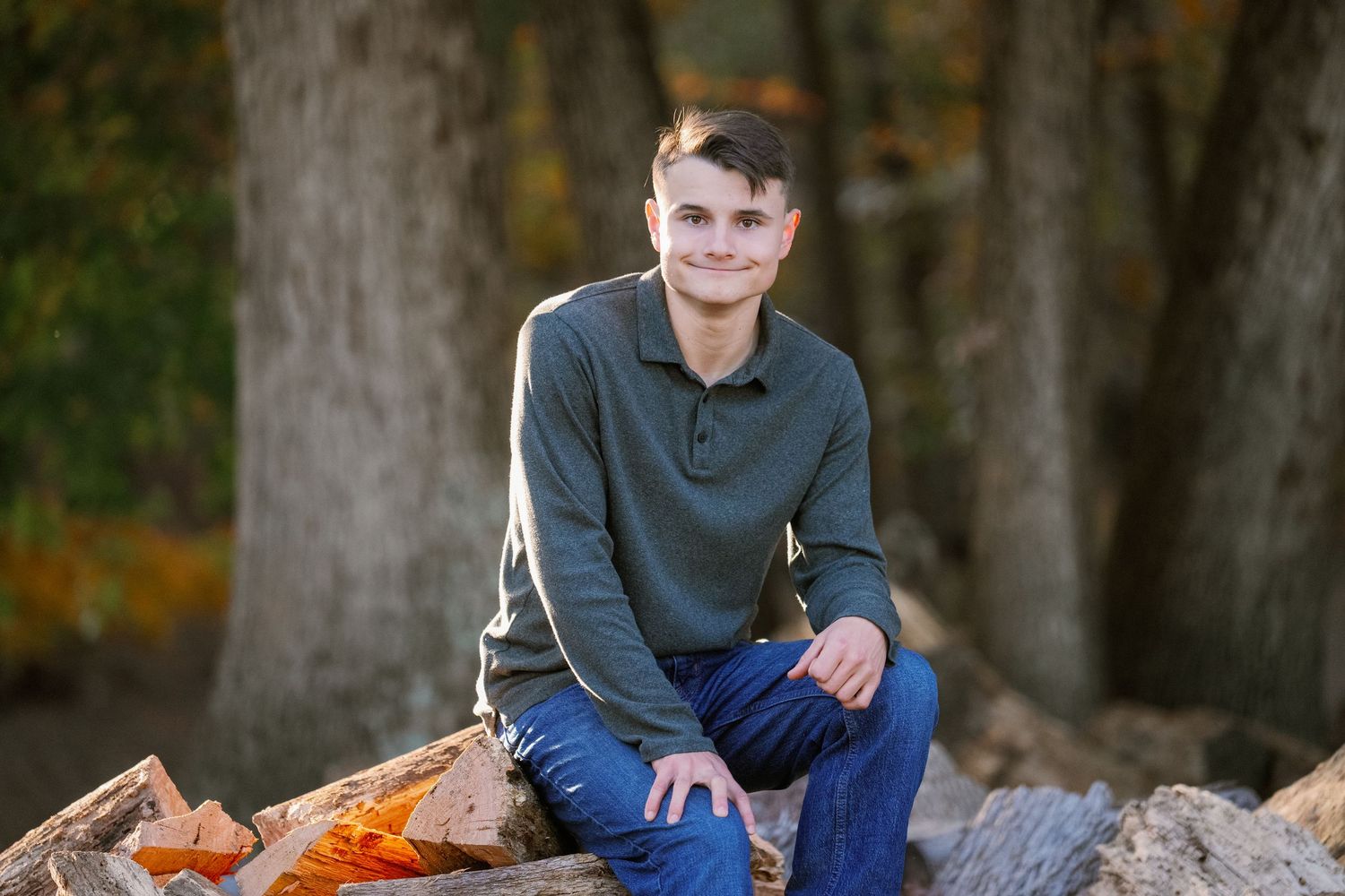 A young person in casual attire poses for portraits on fallen autumn leaves in a wooded outdoor setting.