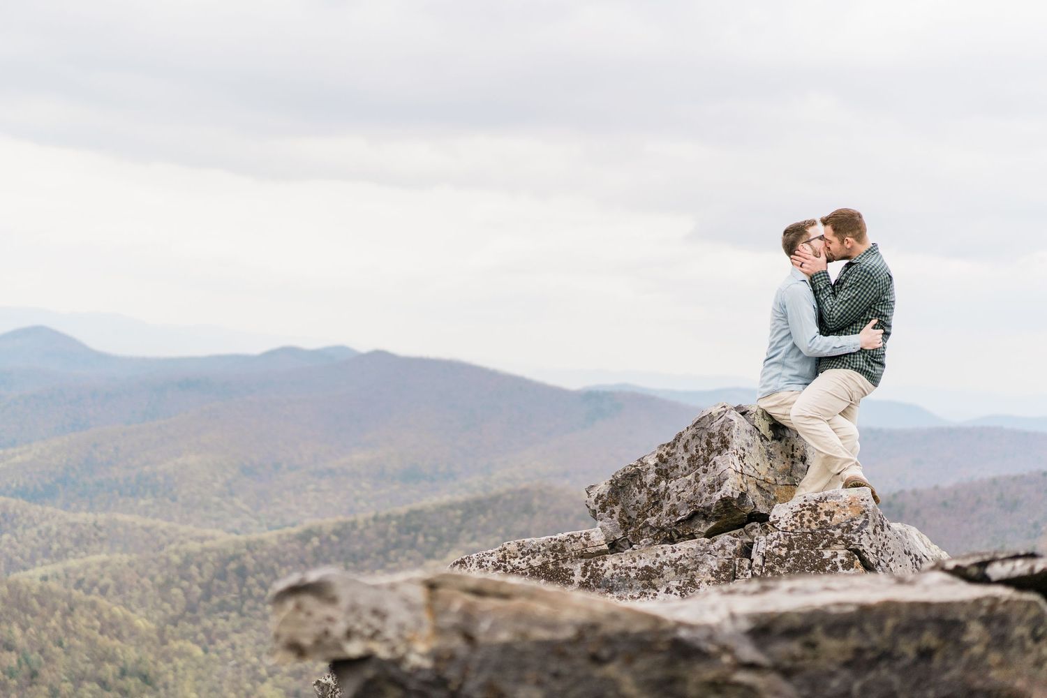 Couple shares intimate moment while sitting on mountain overlook with scenic valley views.