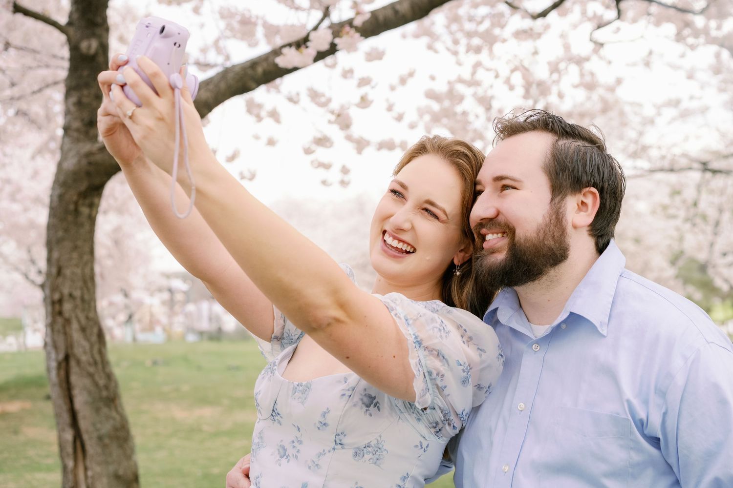 Happy couple taking selfies together under blooming cherry blossom trees in a spring garden.