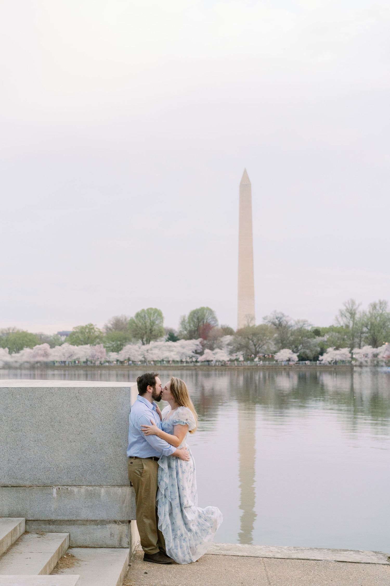 Couple in romantic embrace at Tidal Basin with Washington Monument reflection.
