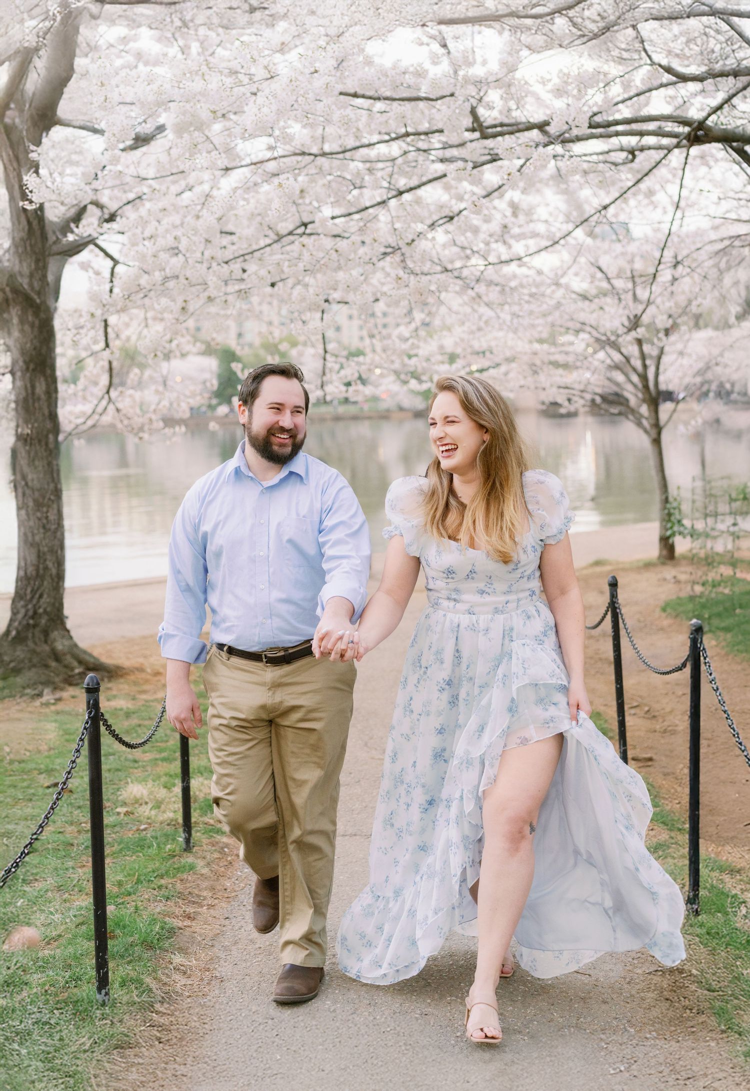 Couple walking under blooming cherry blossoms along Tidal Basin path.