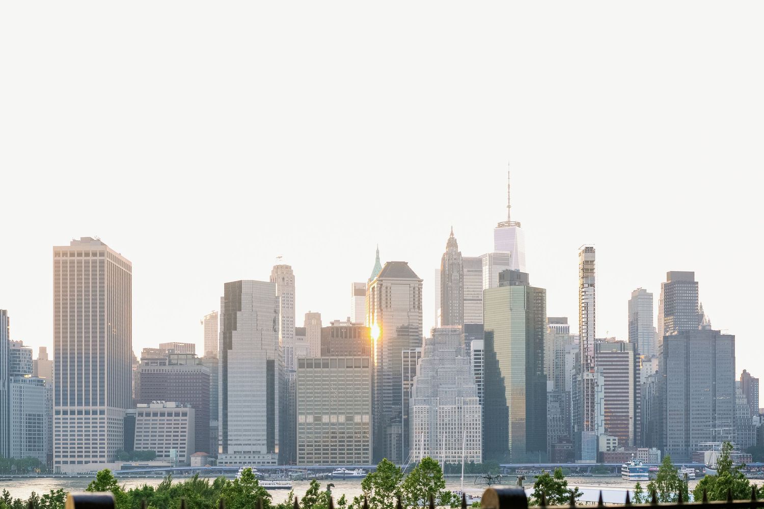 Manhattan skyline viewed across water during golden hour with sun reflecting off skyscrapers.