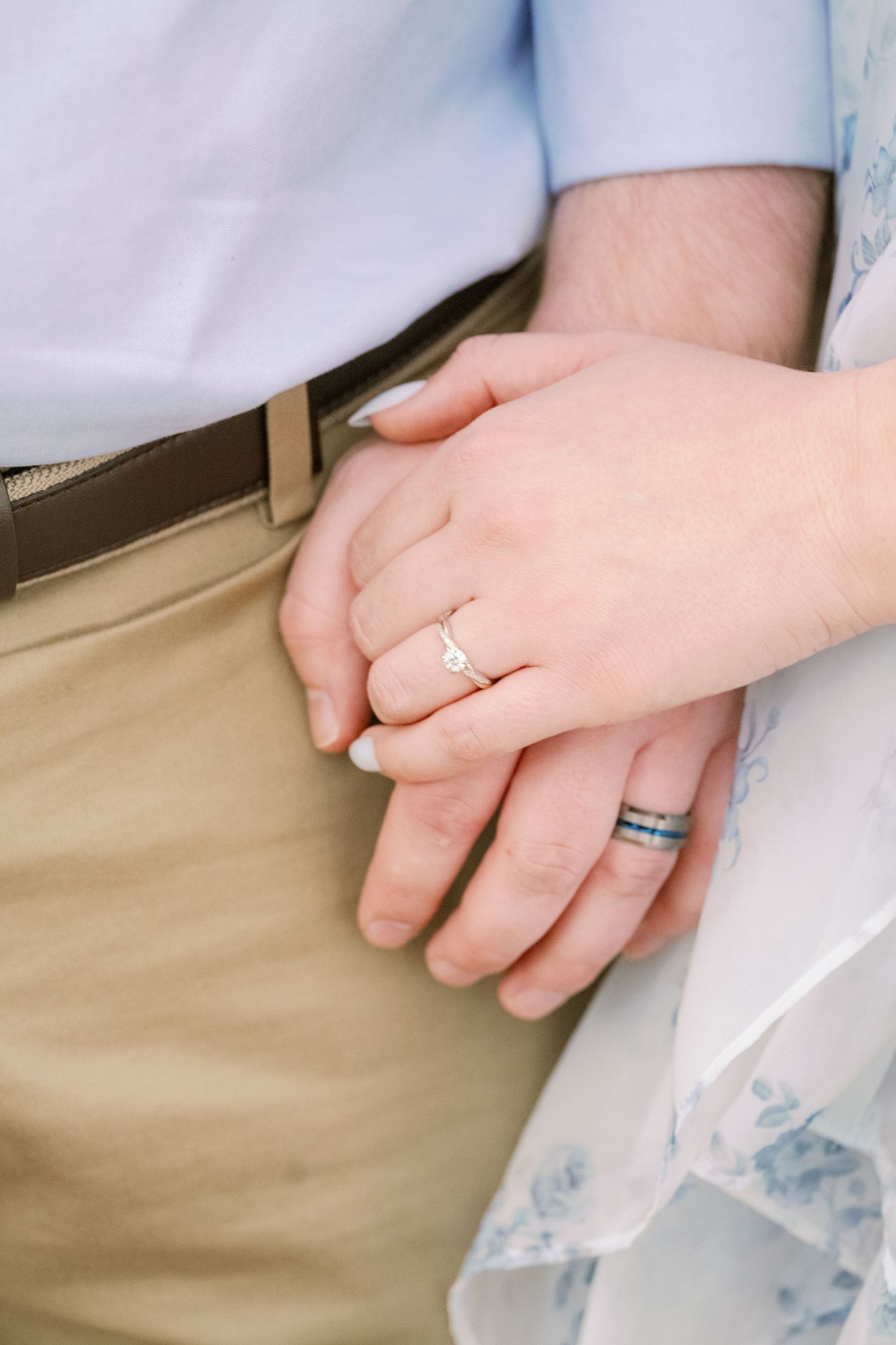 Close-up of engagement rings and holding hands against spring attire.