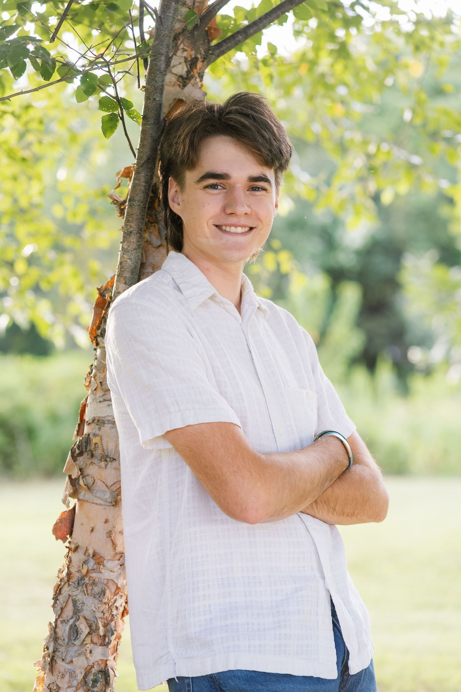 A casual outdoor portrait session in white clothing leaning against a birch tree on a sunny summer day.