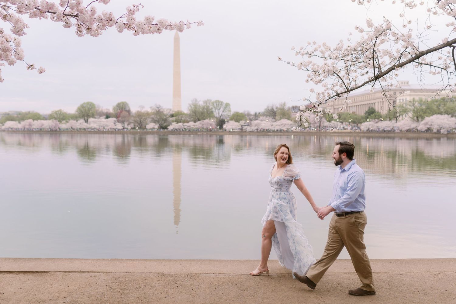 A couple dances along the Tidal Basin shoreline with cherry blossoms and the Washington Monument in view.
