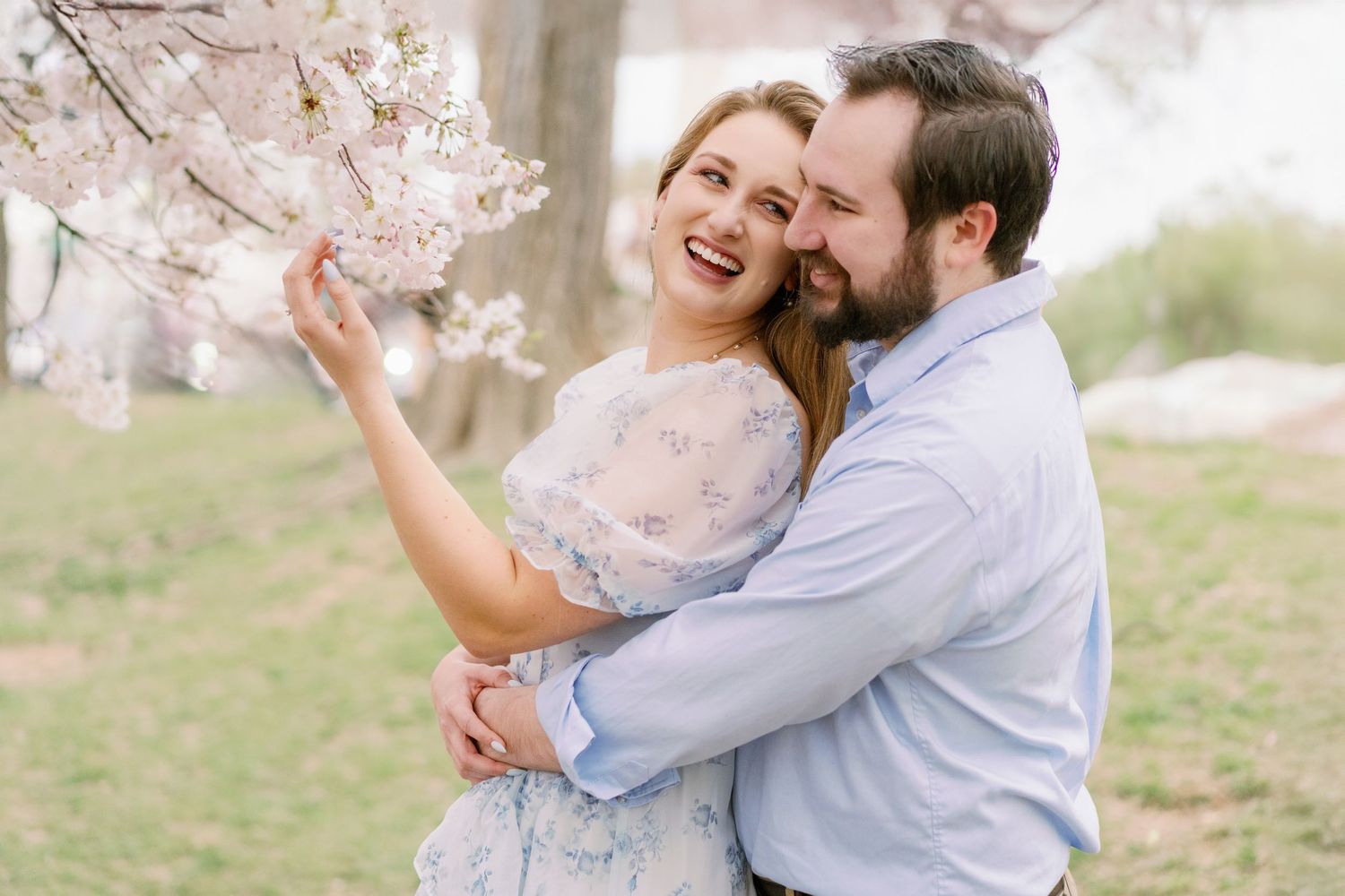 Couple laughing together under blooming cherry blossom trees in springtime.