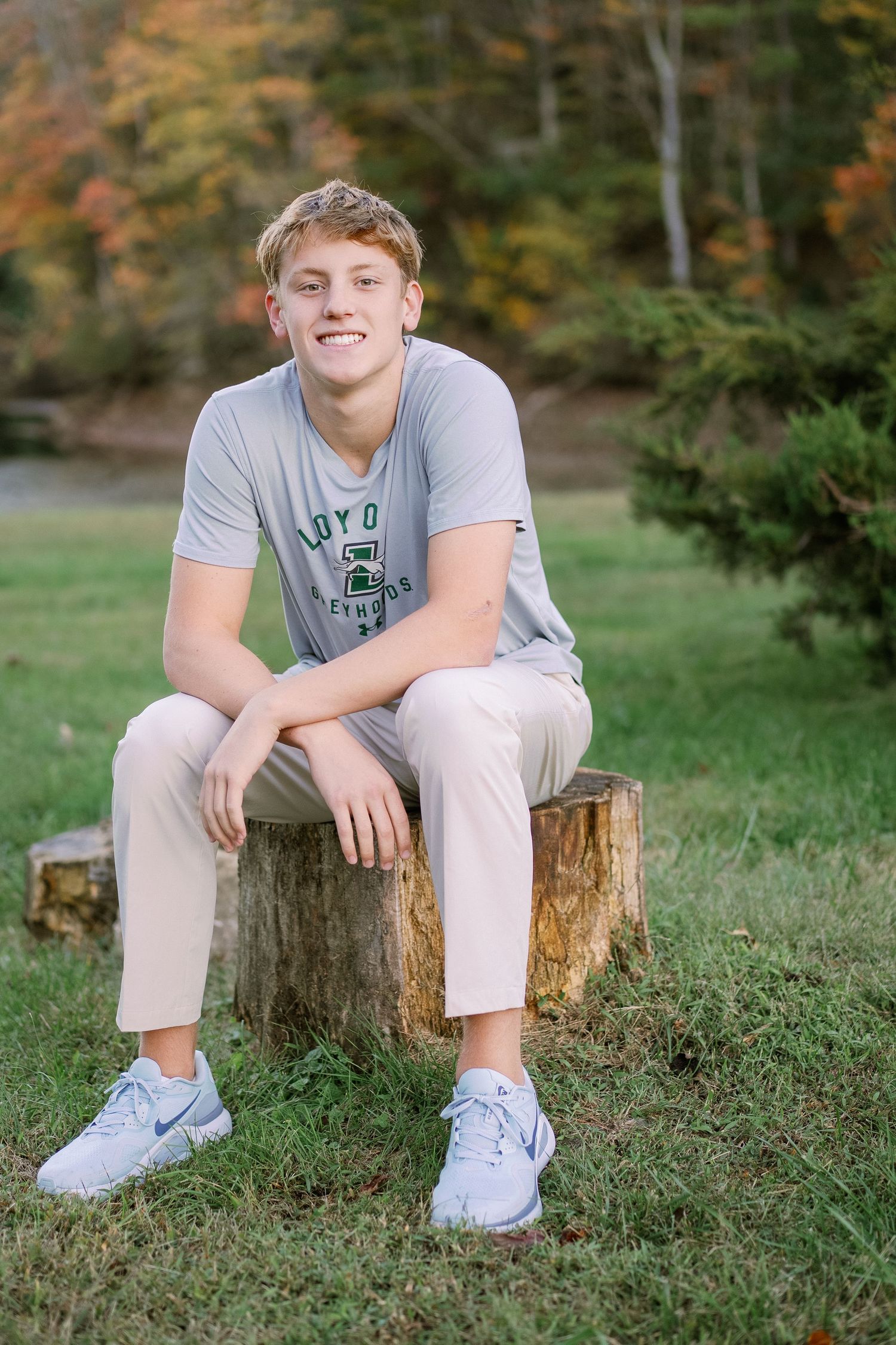 Casual outdoor photoshoot on wooden stumps surrounded by green grass and fall trees.