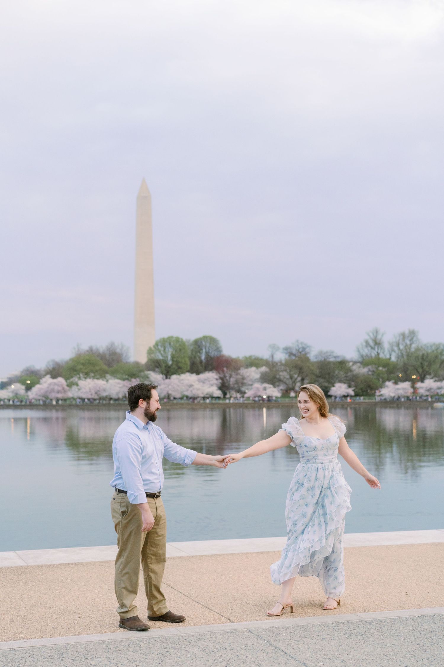 Romantic couple dancing by Tidal Basin with Washington Monument and cherry blossoms.