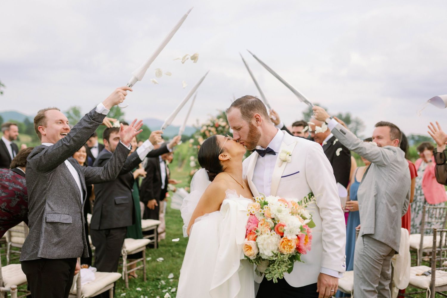 Wedding guests hold sparklers forming an arch for the newlyweds against mountain backdrop.