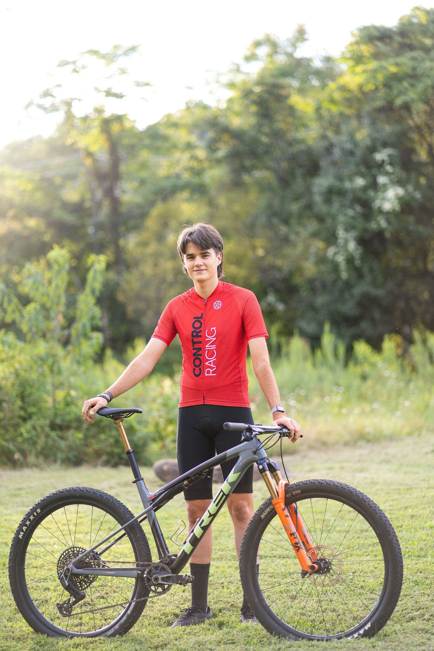 Mountain bike with dark gray frame and orange accents shown from different angles on grassy terrain at sunset.