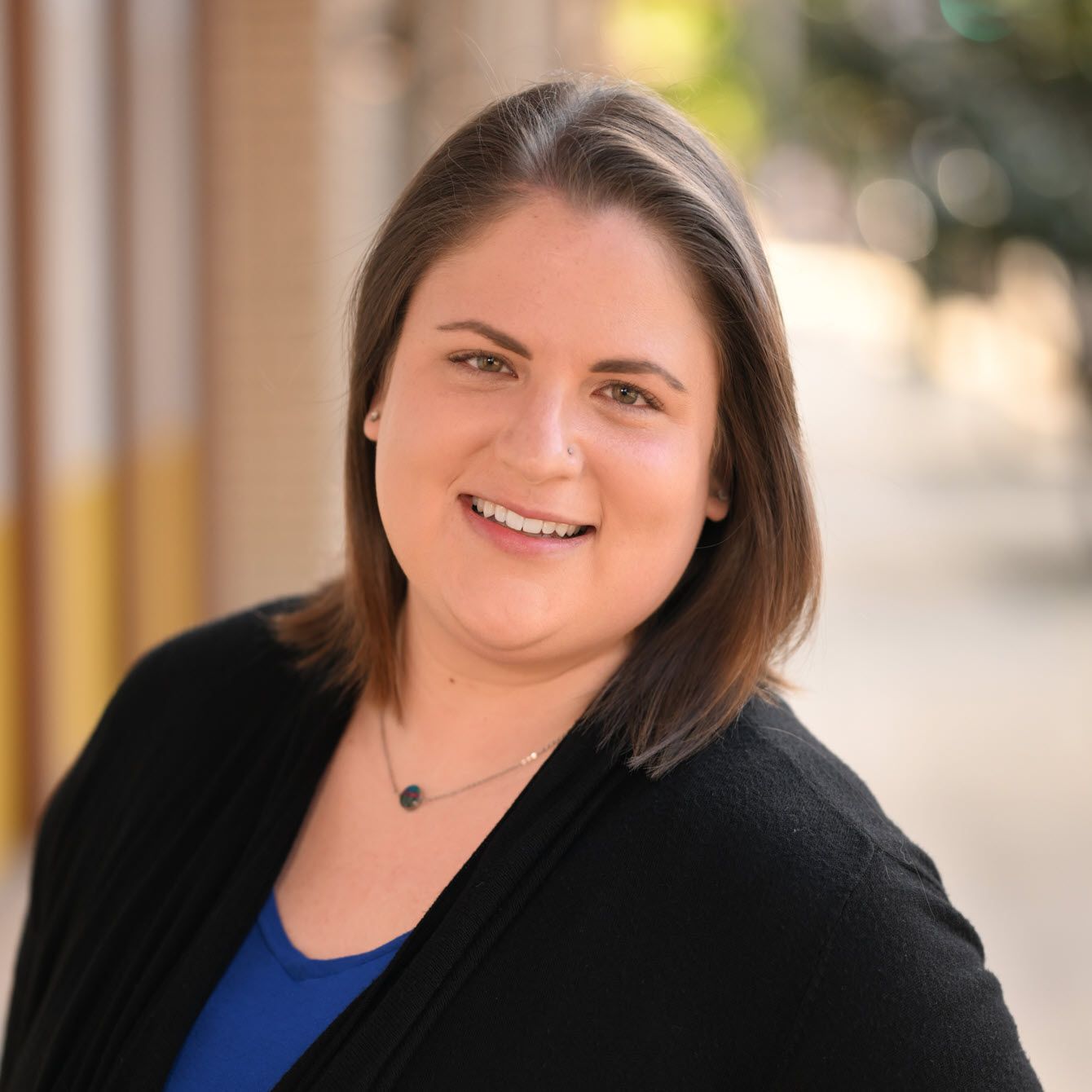 Professional headshot of a businesswoman in a black blazer and blue top against a blurred background.
