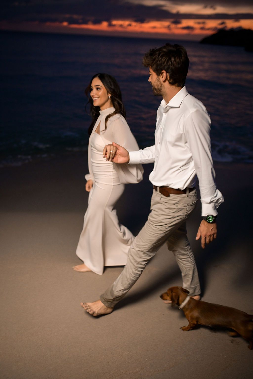 Couple walking with dog on Cala Tarida beach after sunset