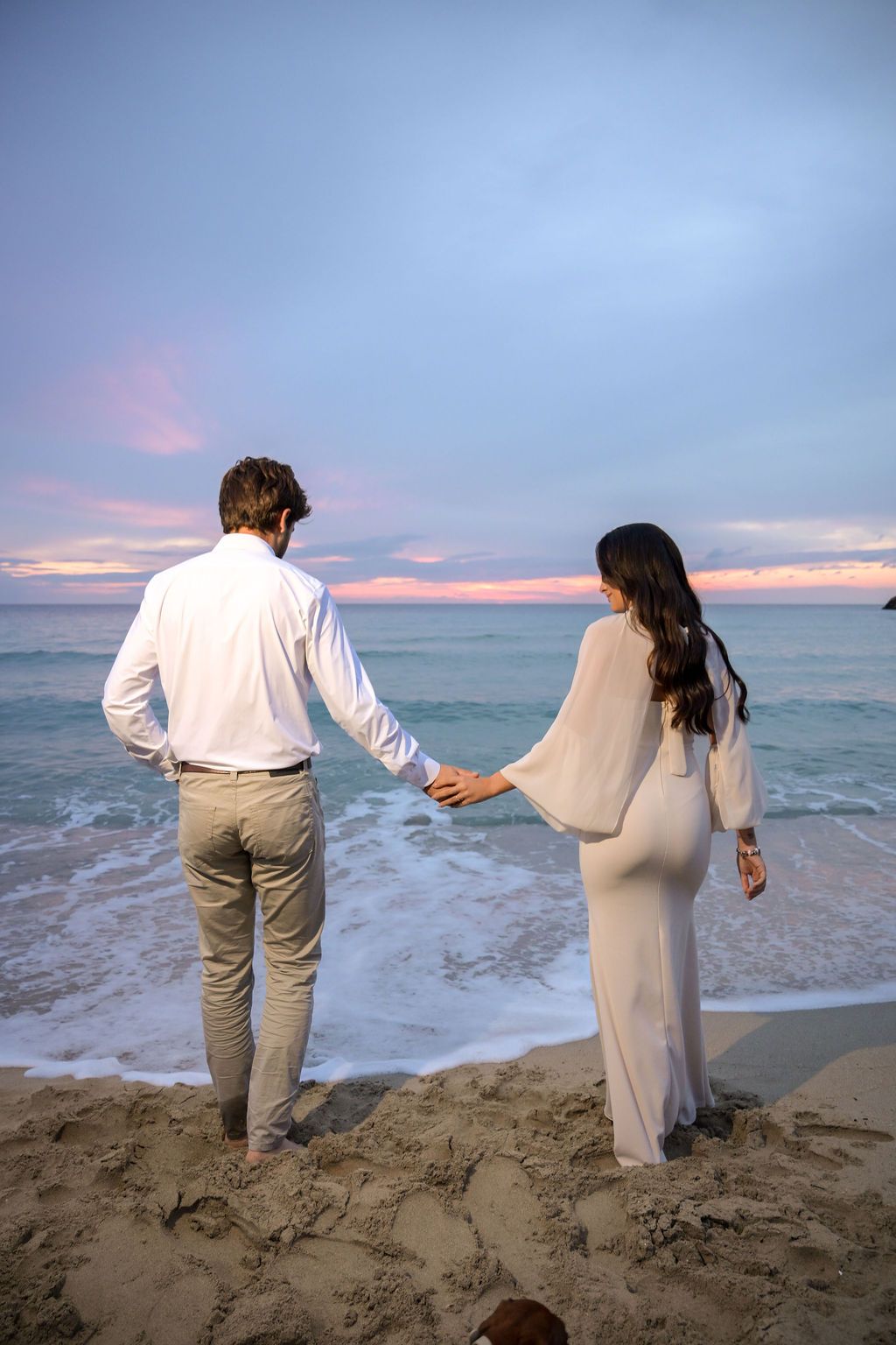 A couple holding hands looking at the waves on the beach in Cala Tarida