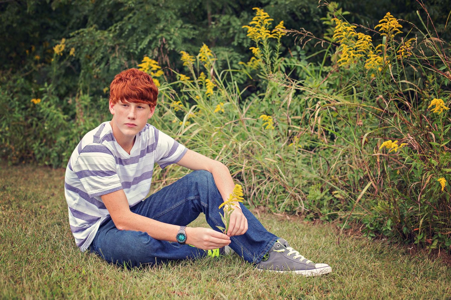 Someone sits casually on grass near blooming yellow wildflowers on a summer day.