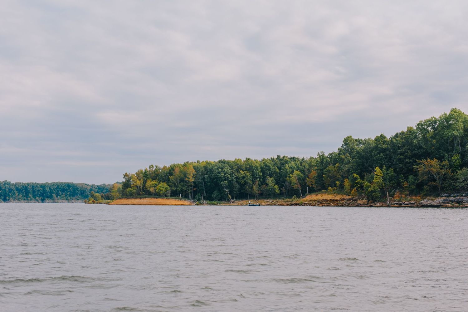 Scenic lake view with forested shoreline and calm waters under an overcast sky during autumn.