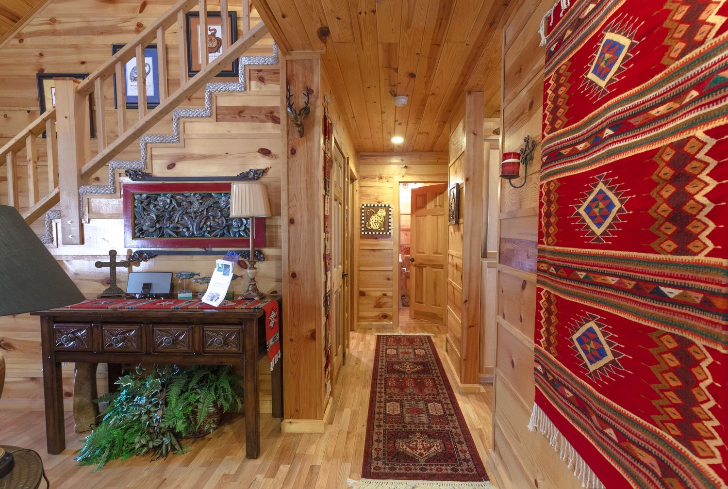 Rustic log cabin hallway with hardwood floors, red Navajo rugs, wood-paneled walls, and Southwest-style decor.