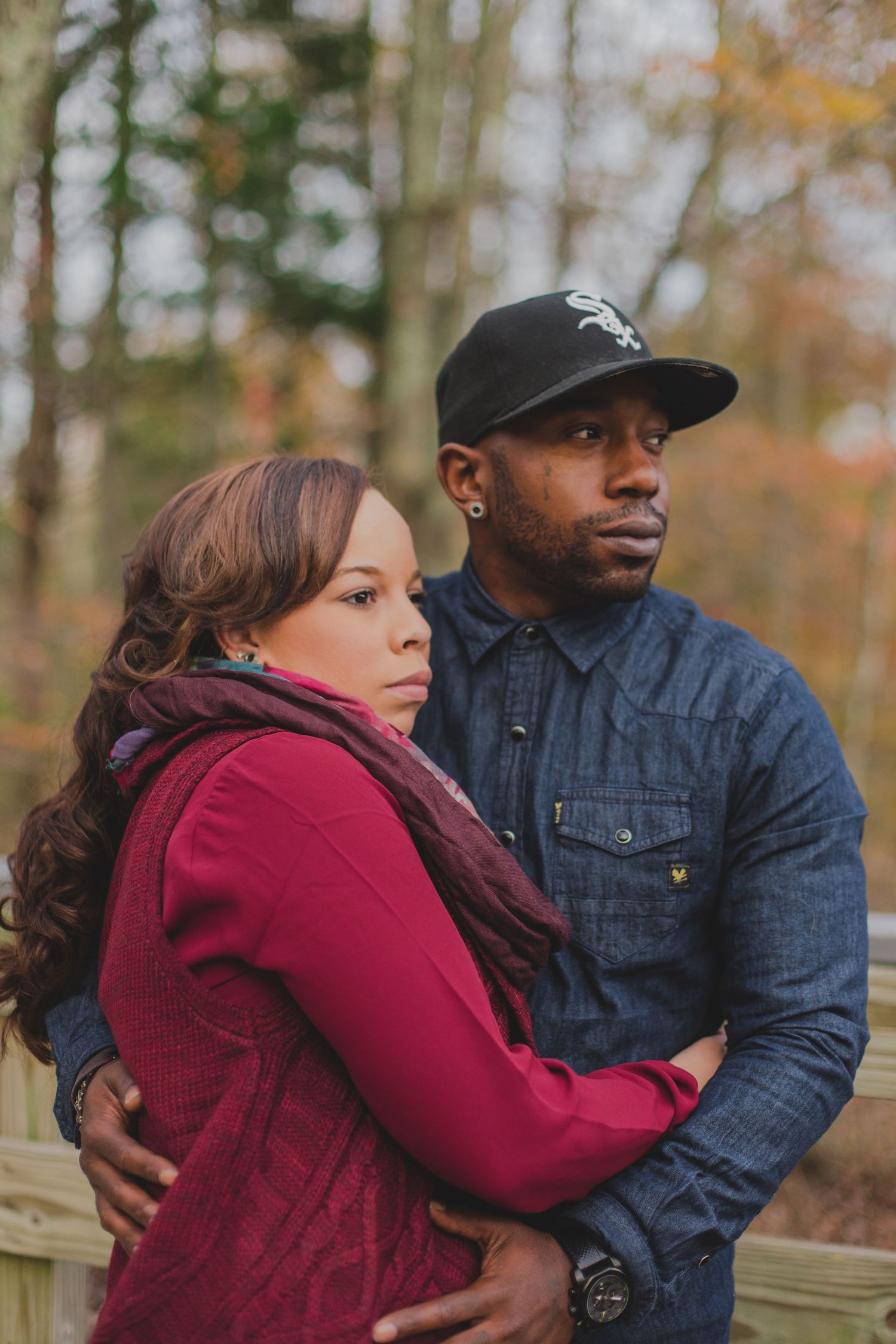 A couple in a romantic embrace outdoors during autumn, with the woman wearing red and the man in denim.