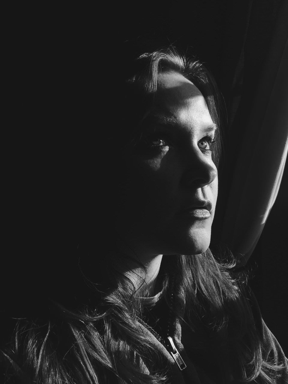 Black and white portrait of a young woman gazing upward in dramatic chiaroscuro lighting against a dark background.