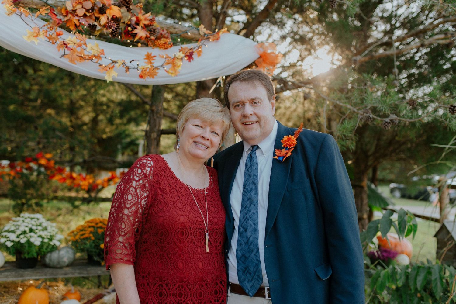 Couple smiling at outdoor fall wedding ceremony with autumn leaves and orange floral decorations.