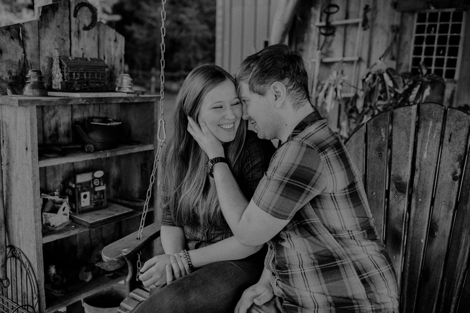Black and white photo of a romantic couple sharing a tender moment on a rustic wooden bench in a vintage shed.