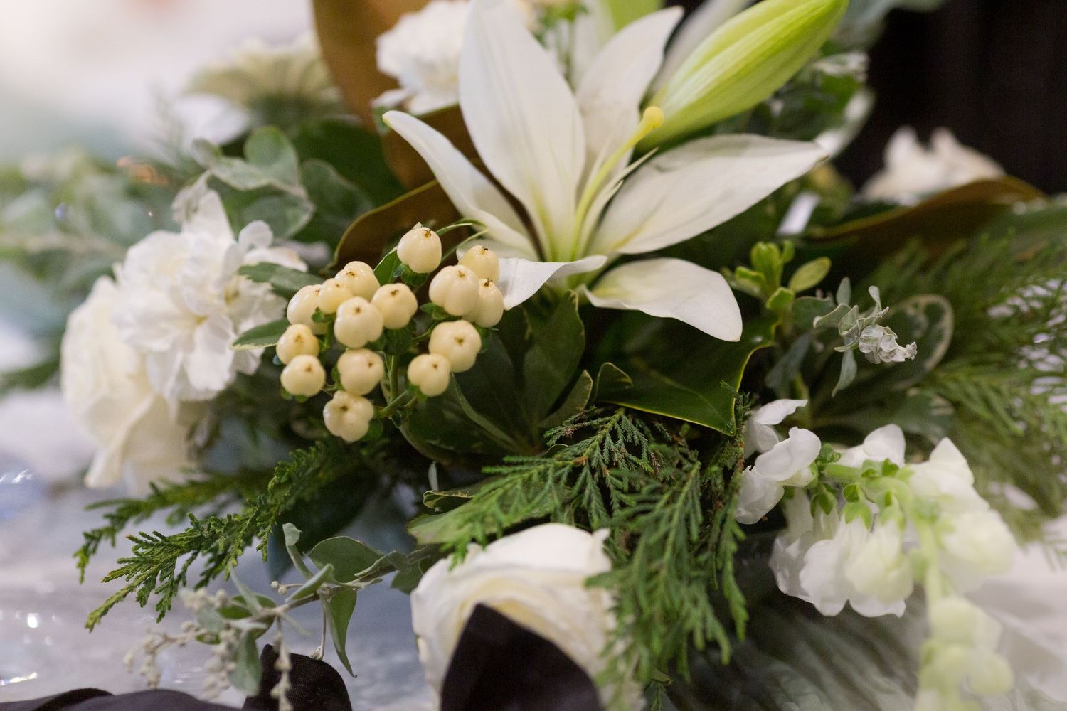 Close-up of elegant white lilies and greenery in a wedding floral arrangement with delicate pearls and decorative details.