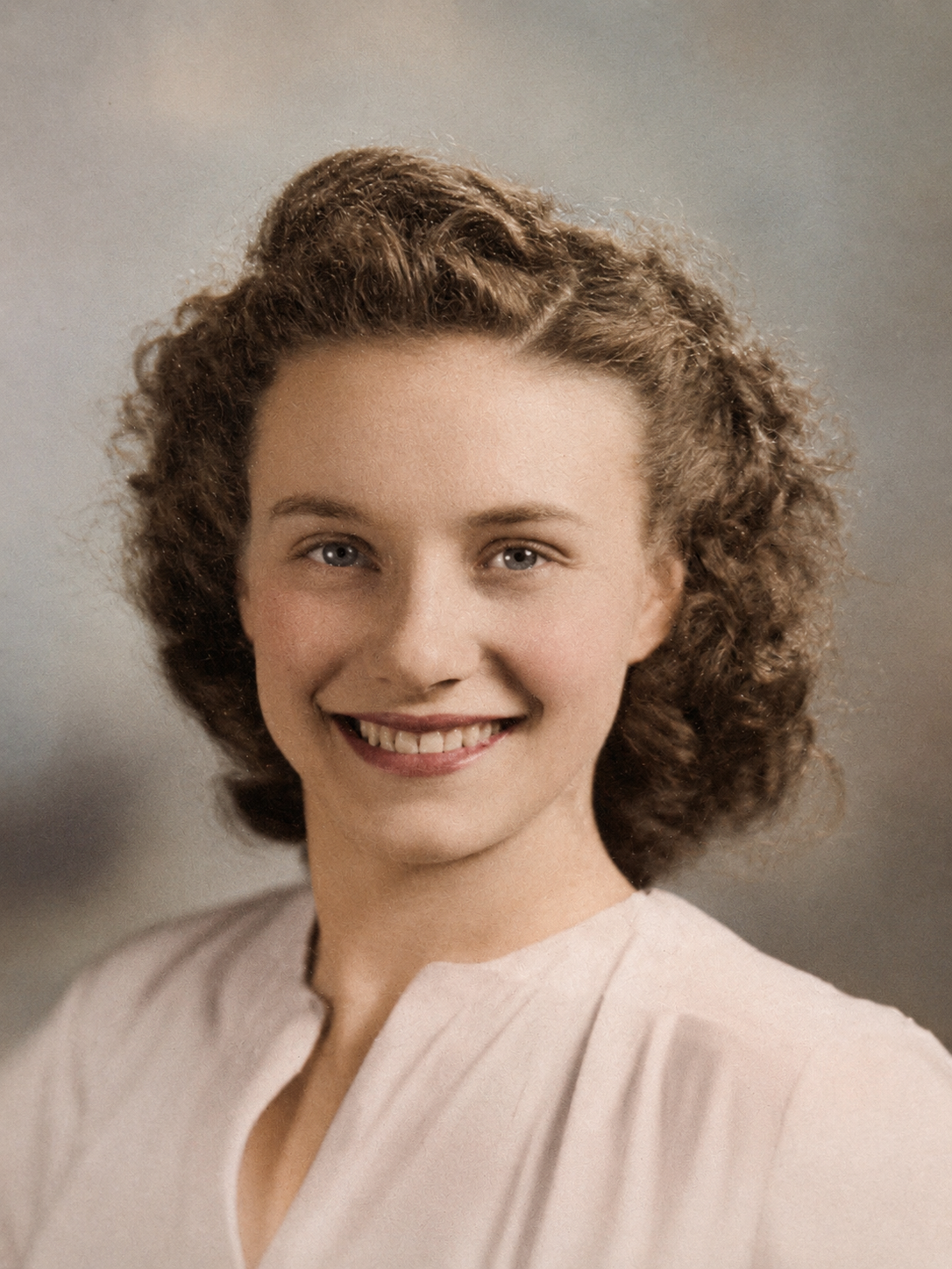 Vintage color portrait of a young woman with curly brown hair and a warm smile, wearing a light pink blouse.