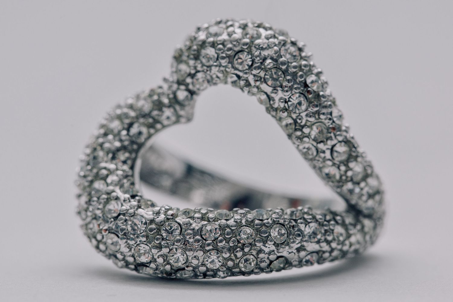 Heart-shaped diamond pavé ring in white gold, encrusted with sparkling round-cut diamonds on a gray background.